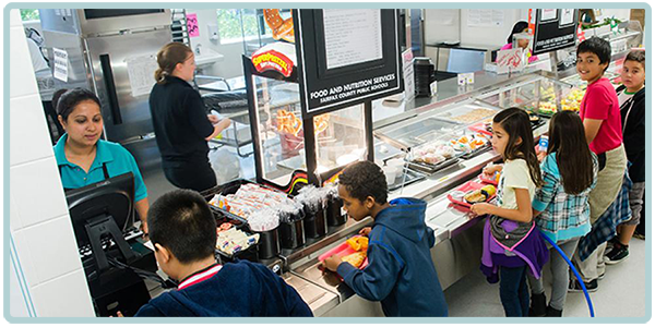 Kids going through cafeteria line holding food trays.